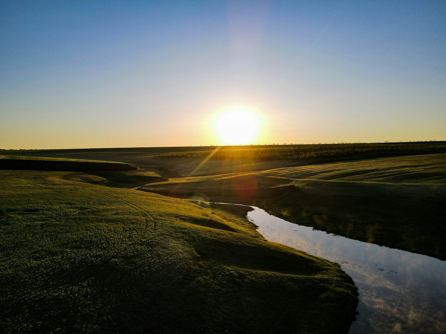 El sol sale sobre un río sinuoso que atraviesa campos verdes.