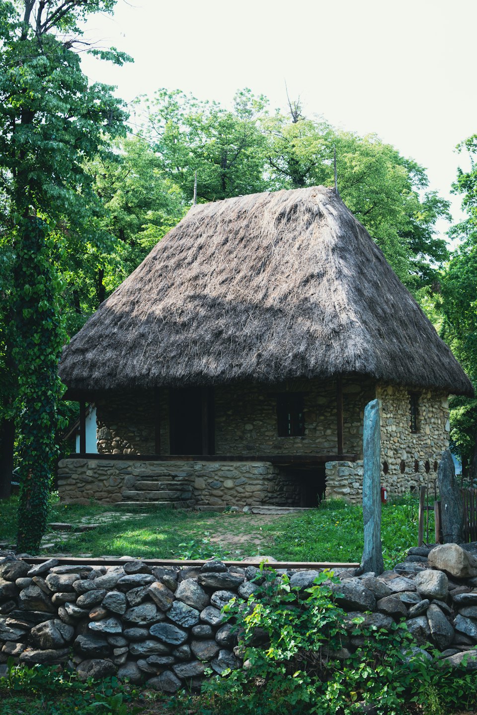 Casa tradicional de piedra con tejado de paja entre el follaje.