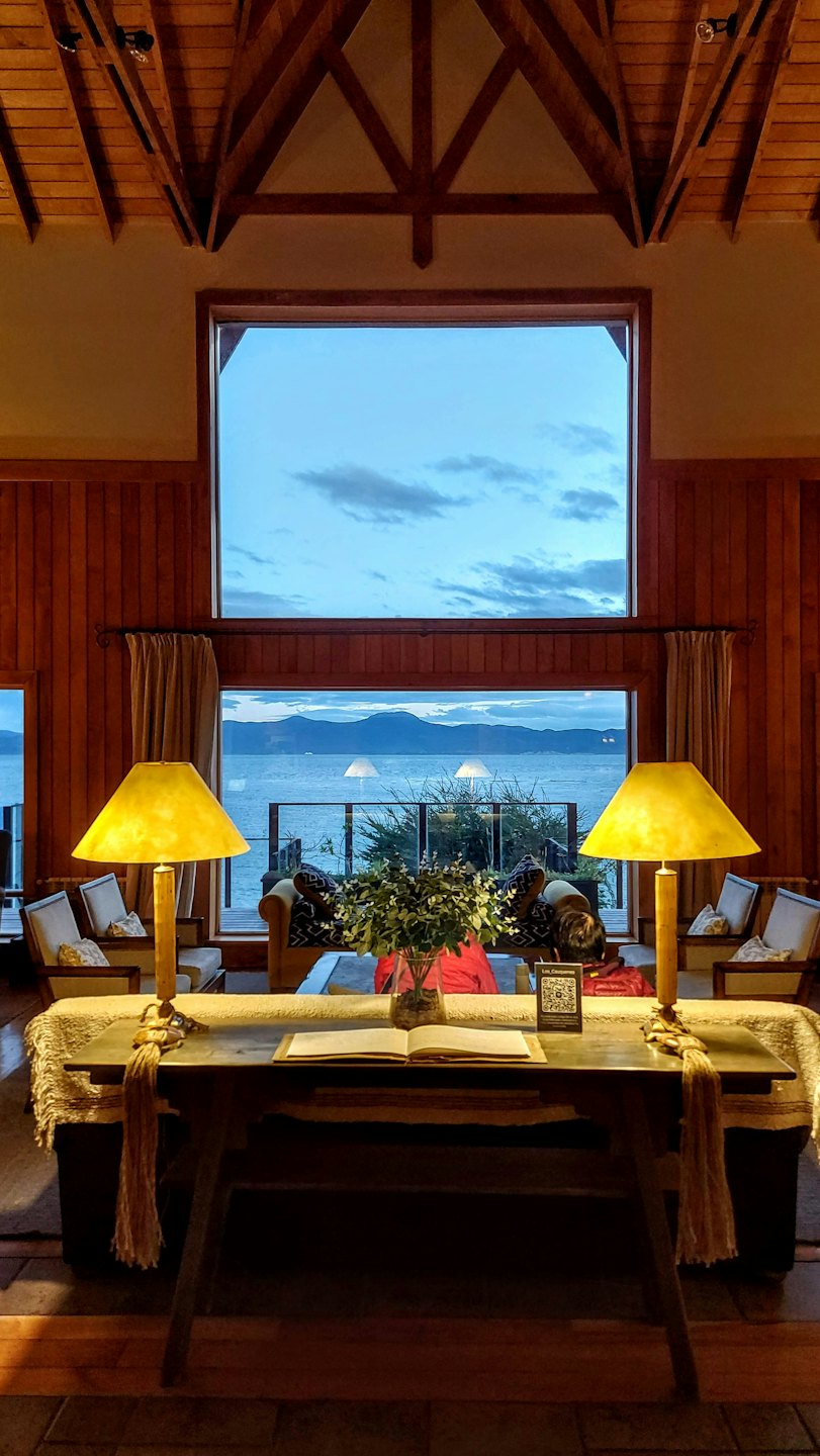 Interior acogedor de una cabaña con una mesa puesta junto a un gran ventanal con vistas a un lago.